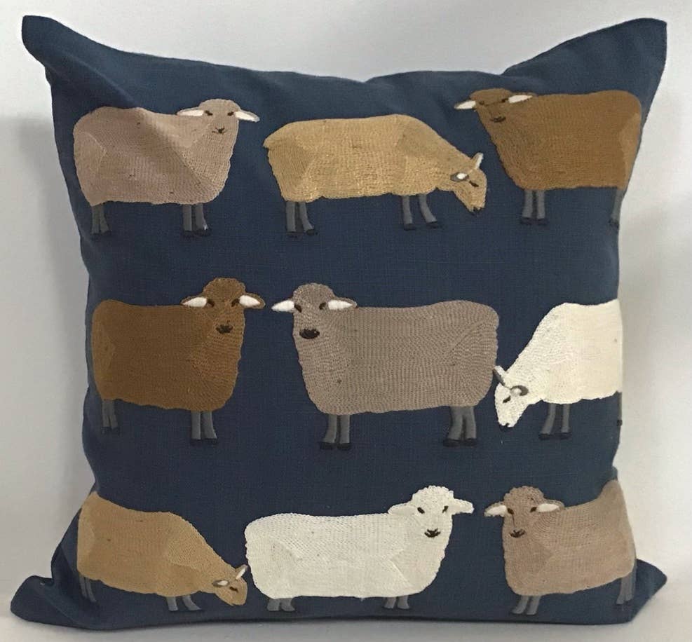 Square navy cotton pillow embroidered with sheep in tan, gold, brown, white and gray in rows