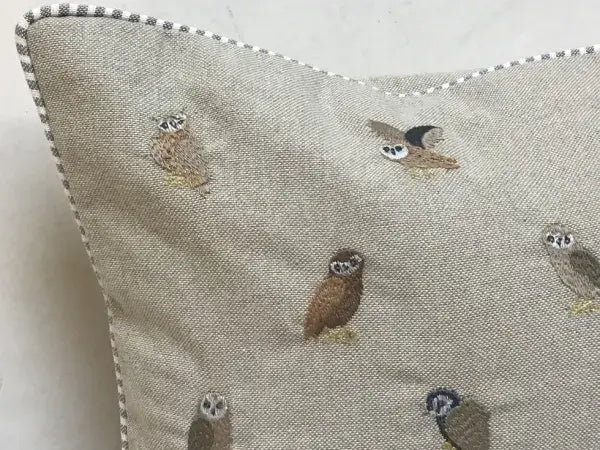 Close-up of a cotton pillow corner with embroidered owls in brown, gray and tan, and black and white striped piping