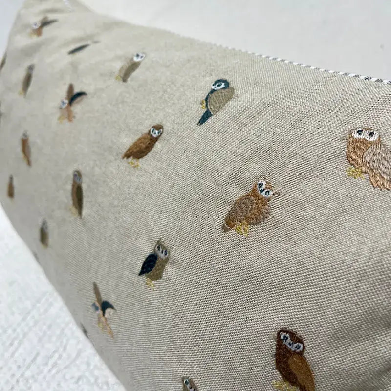 Close-up of a cotton pillow with embroidered owls in brown, teal, gray and tan, with striped piping at the edge