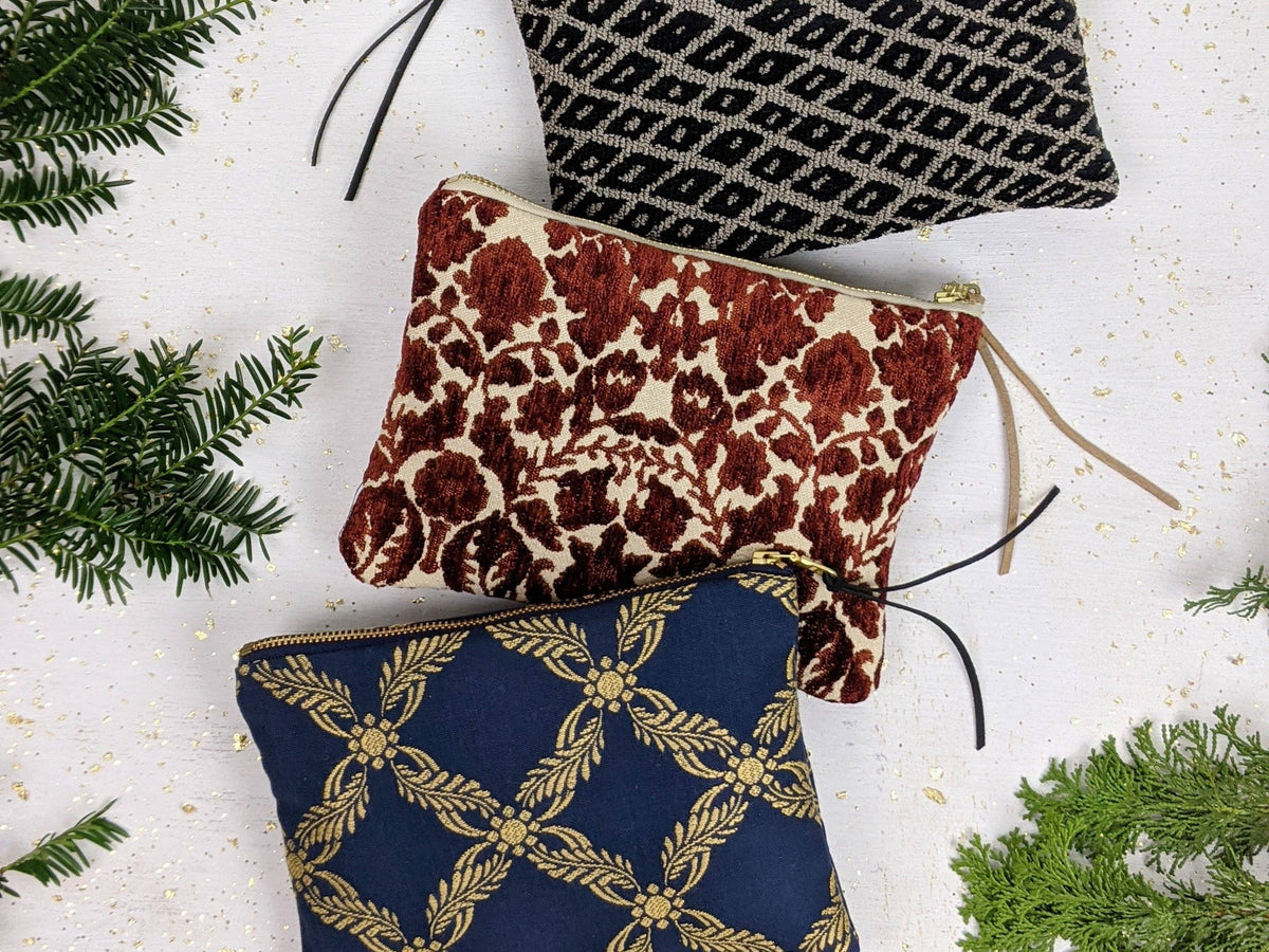 Three pouches grouped together: the black and taupe Black Diamond Needlepoint pouch, a rust floral velvet pouch, and a navy and gold trellis-print pouch