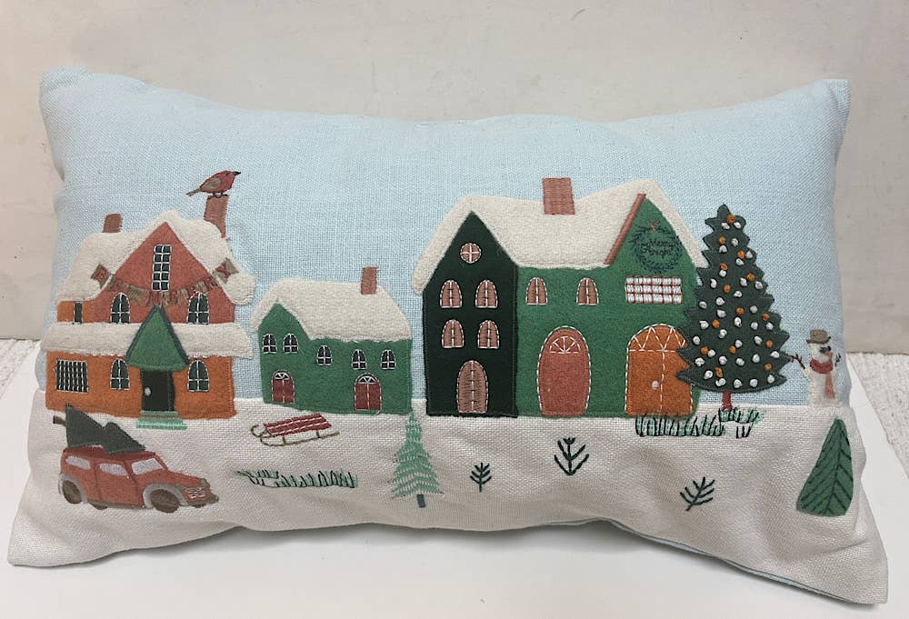 Rectangular pale blue cotton pillow with an appliqued snowy village of orange and green houses, a woody car and a tree