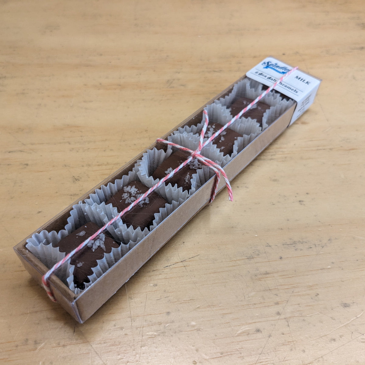Milk chocolate sea salt caramels in paper cups in a long kraft box tied with red and white twine