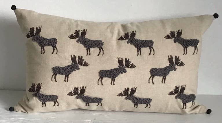 Rectangular beige cotton pillow with embroidered gray french-knot moose in rows and black pom-poms at the corners
