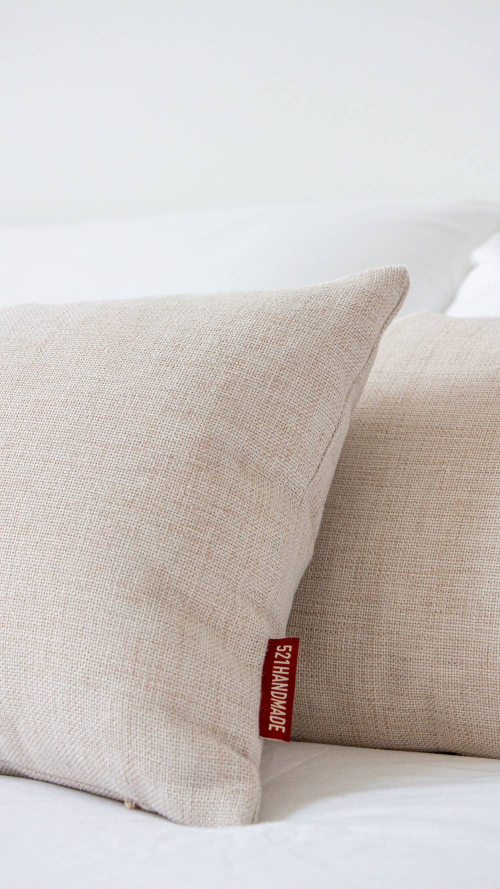 Close-up of two natural linen lumbar pillows stacked on a white bed, showing the red 521handmade fabric tag on the corner