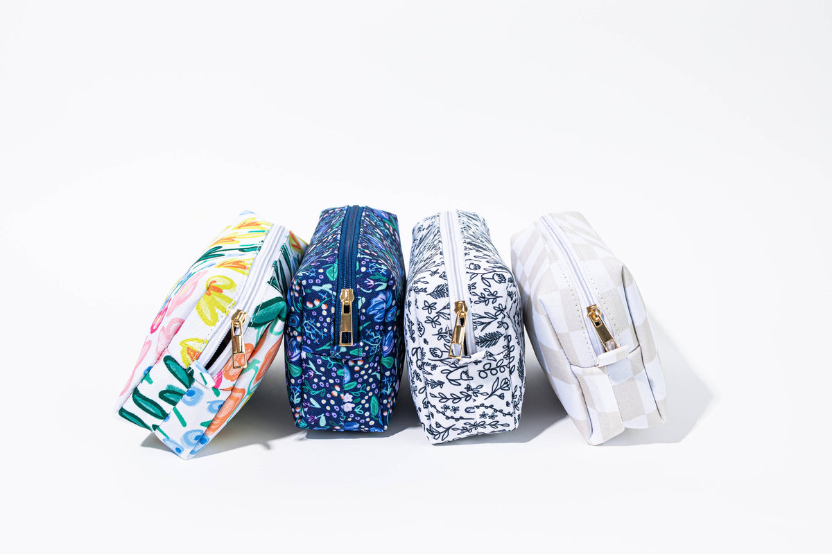 Alison Floral Zipper Pouch in navy blue floral standing in a row with three other boxy zip pouches in multicolor floral, black and white floral, and gray gingham prints