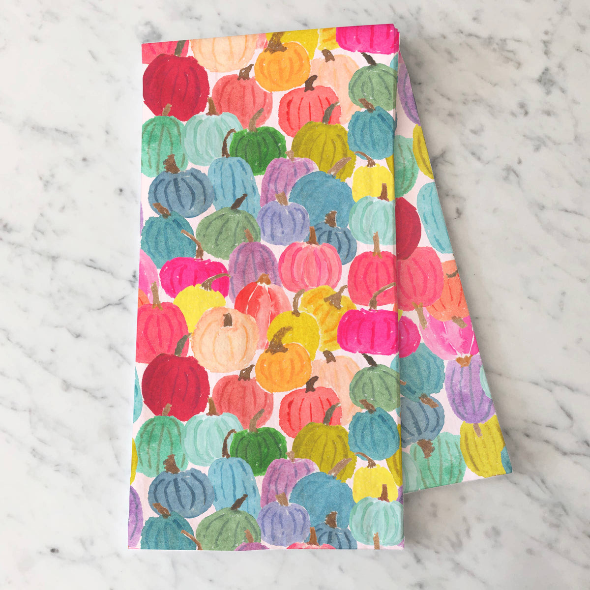 Colorful Pumpkins tea towel folded on white marble showing the rainbow watercolor pumpkins