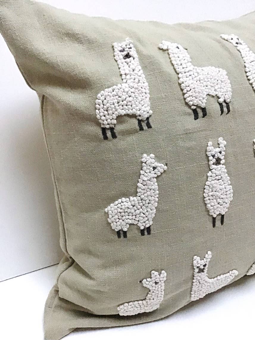 Angled close-up of a sage green pillow embroidered with cream french-knot llamas with dark legs