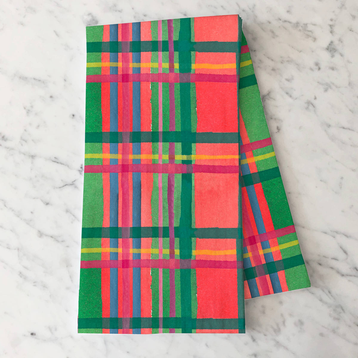 Holiday Plaid tea towel folded on white marble, with a red, green, pink and blue watercolor plaid