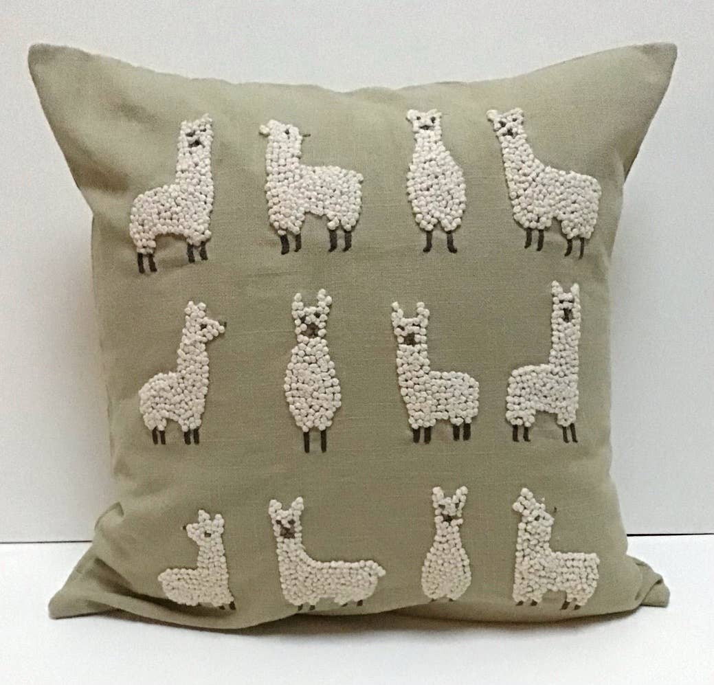 Square sage green cotton pillow with twelve cream french-knot llamas standing and sitting in three rows