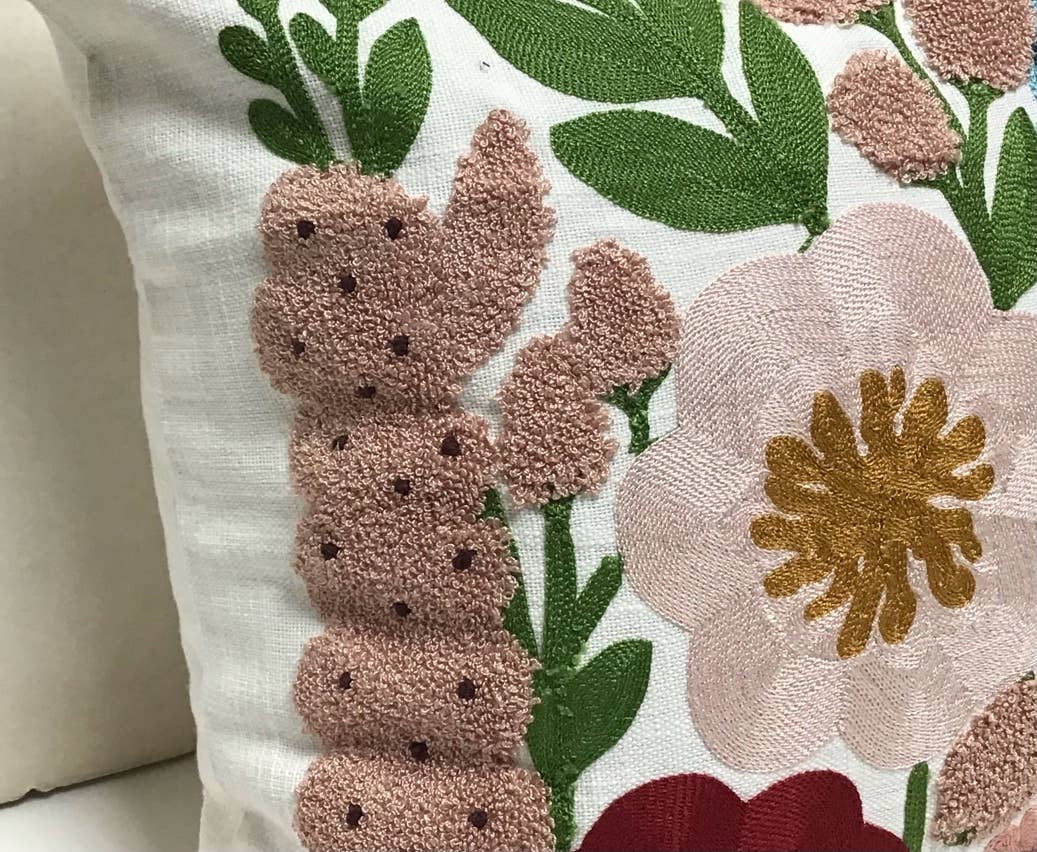 Close-up of a white pillow with tufted mauve foxglove blooms, a blush flower with a mustard center and green leaves