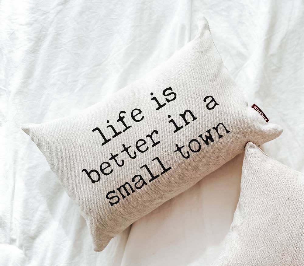Life is Better in a Small Town Linen Pillow angled on a white bed next to a plain natural linen pillow, close alternate crop