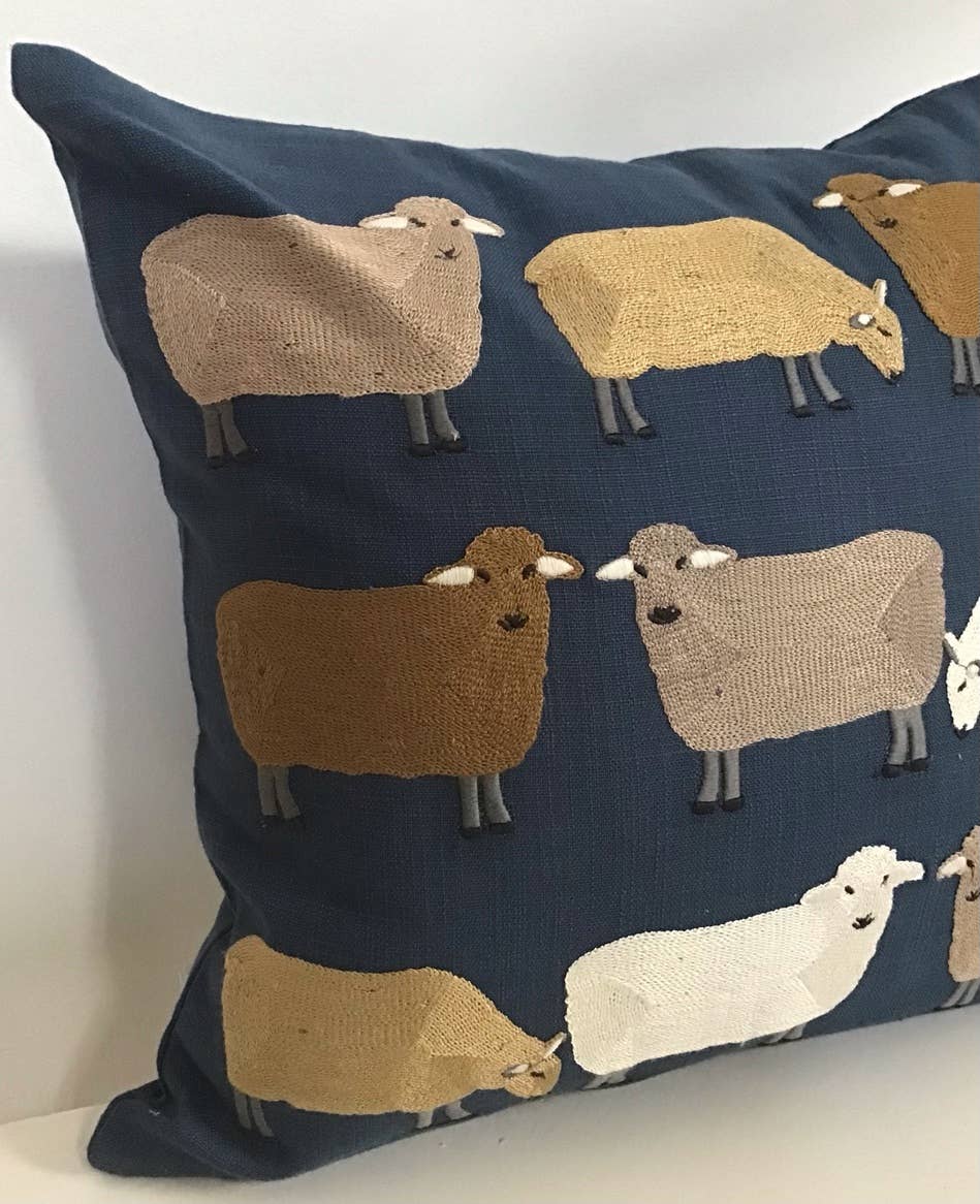 Close-up corner of a navy cotton pillow embroidered with sheep in tan, gold, brown and white, with gray legs