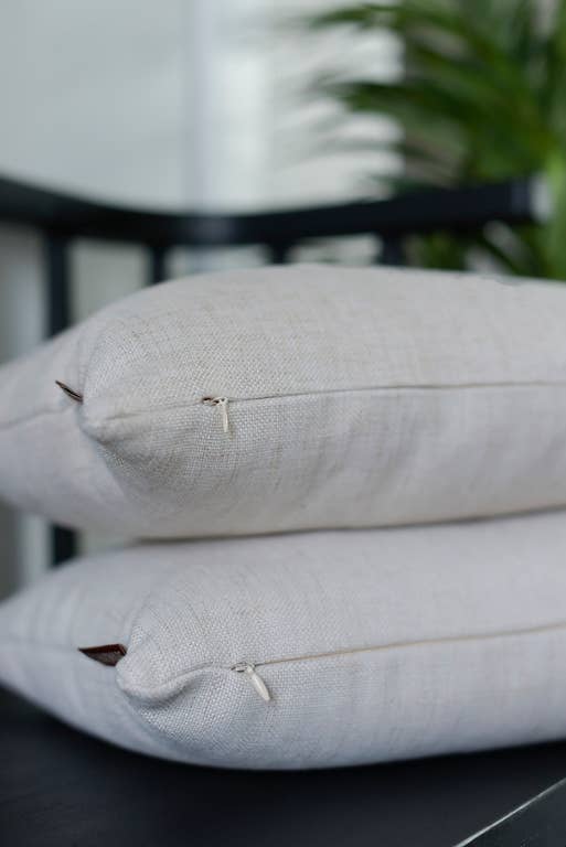 Close-up of two natural linen lumbar pillows on a black stand near a green plant, showing the pillow corners and stitched seams