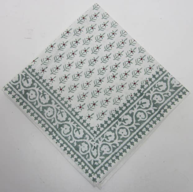 Folded cotton napkin block-printed in sage green with a leafy sprig pattern, red dots and a scrolled border, on white