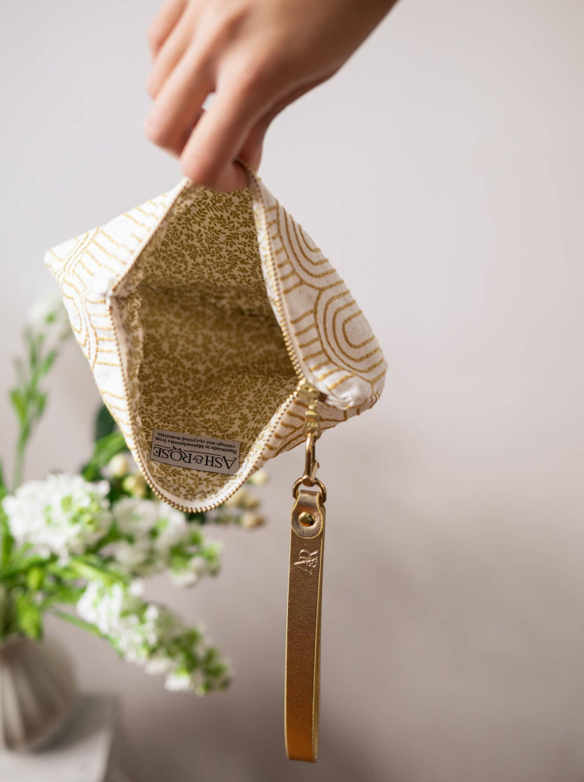 Open Josephine Clutch wristlet purse showing a gold patterned lining and the Ash & Rose label, gold Art Deco arch embroidery exterior, gold leather strap