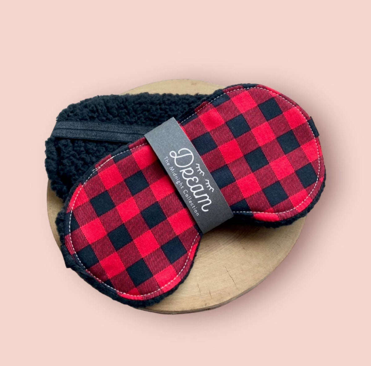 Red and black buffalo check Dream sleep mask with black sherpa edging and a Midnight Collection band, on a blush backdrop