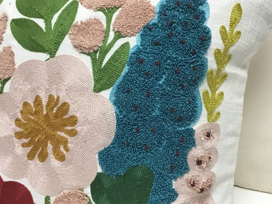 Close-up of a white pillow with a tufted teal flower spike, a blush bloom with a mustard center and green leaves