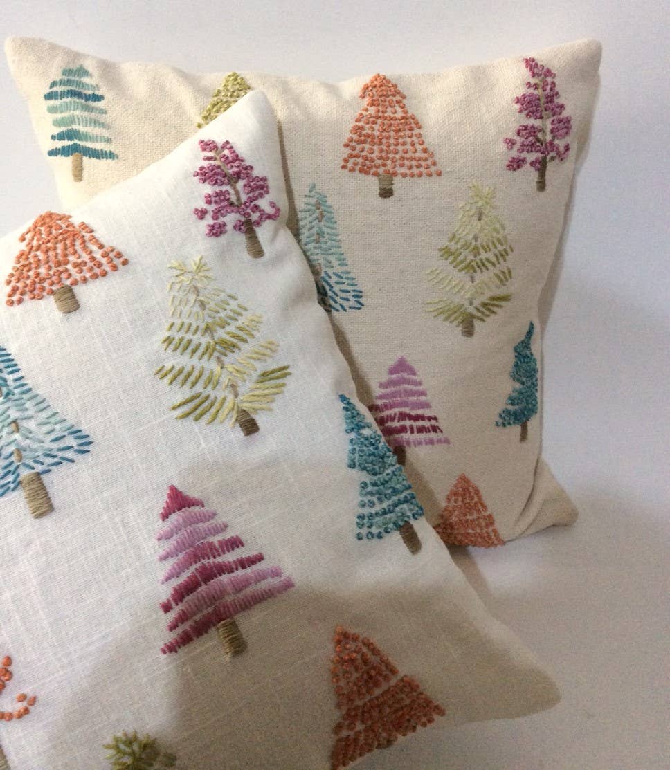 Two cream cotton pillows with embroidered stitched pine trees in pink, teal, olive, orange and magenta, stacked together
