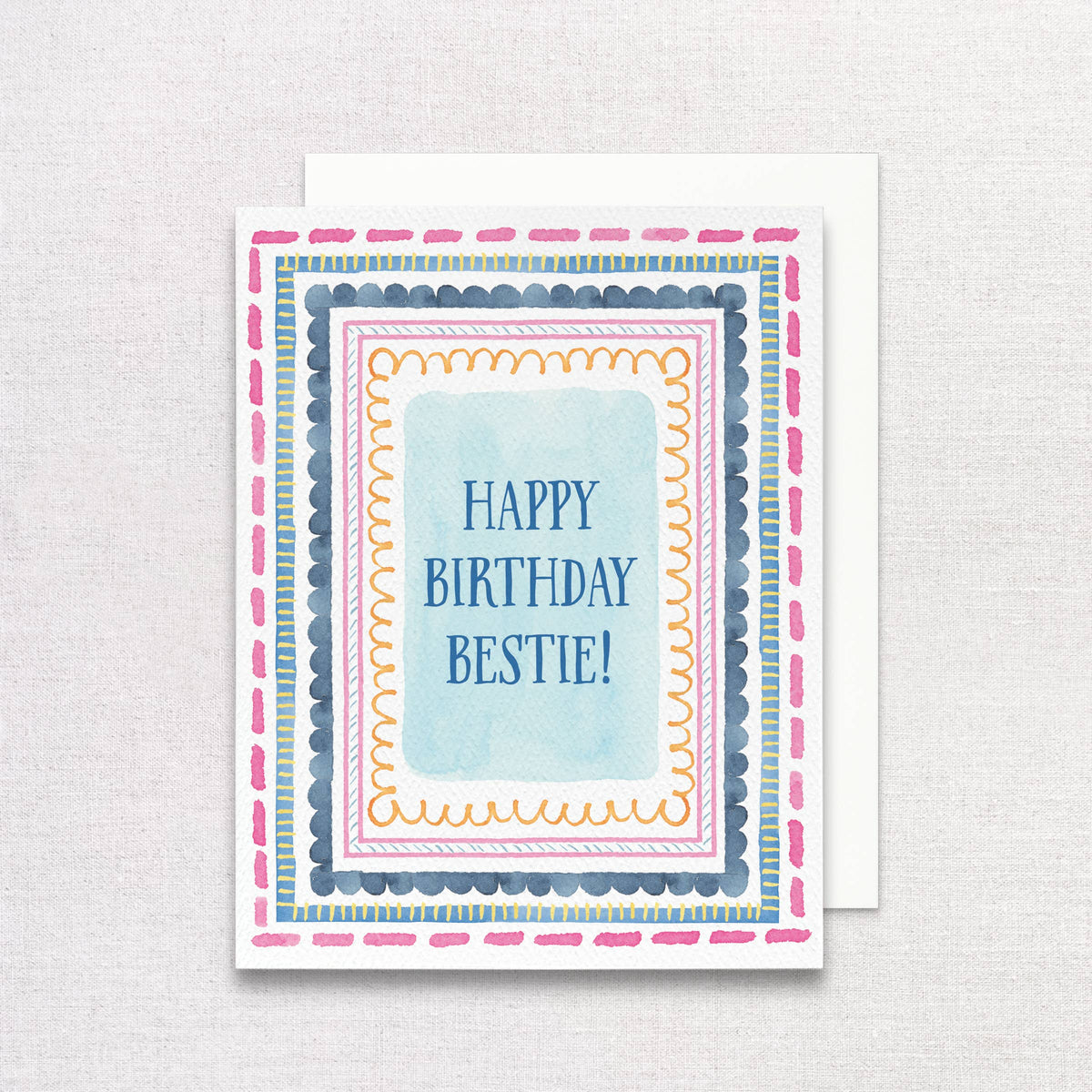 Happy Birthday Bestie card with watercolor borders, on a white envelope over linen