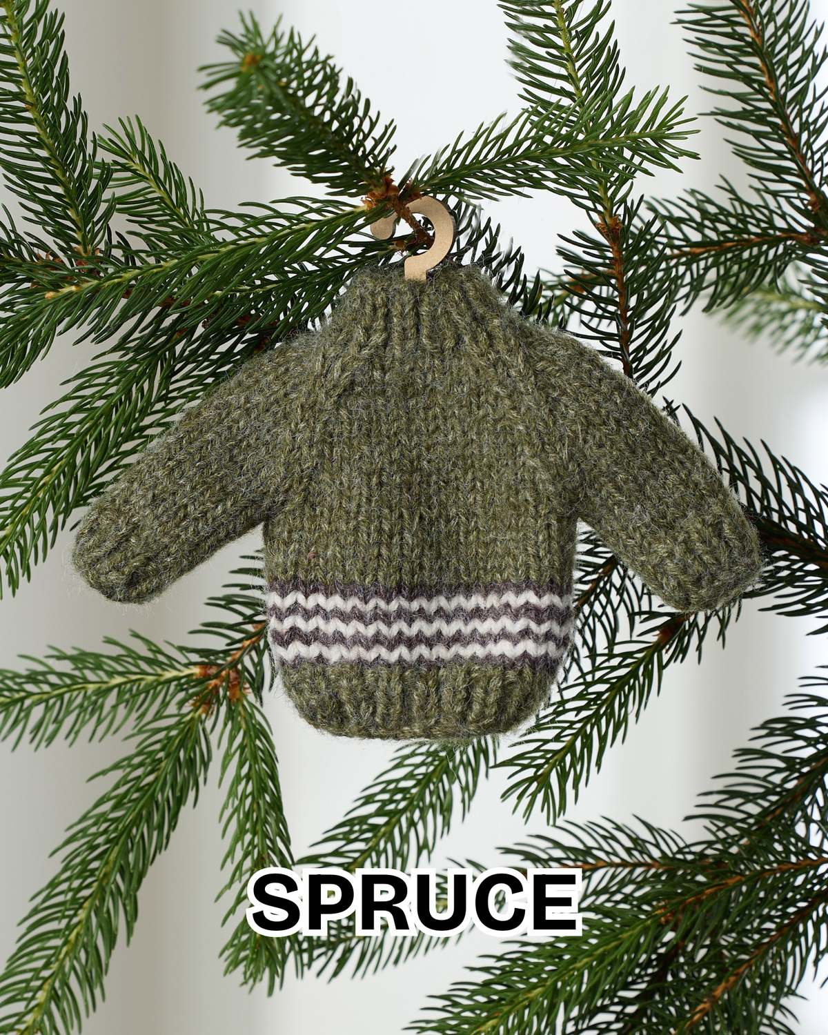 Spruce green mini knit sweater ornament hanging on an evergreen branch