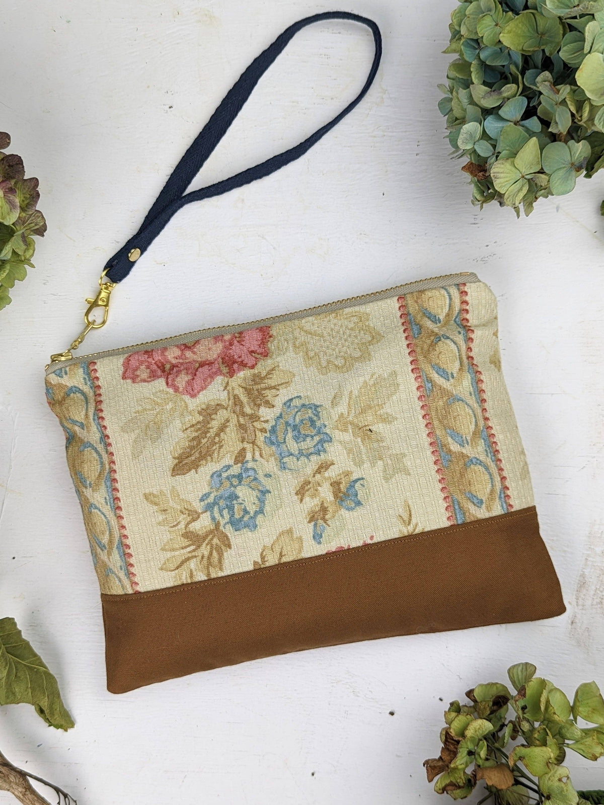 Antique Roses wristlet purse laid flat, ivory fabric with blue and pink floral pattern, tan leather bottom, navy wristlet strap
