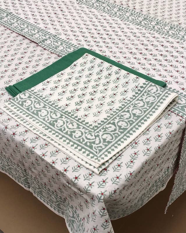 Block-printed cotton napkin with sage green sprigs and a green border, laid on a matching tablecloth with a green edge