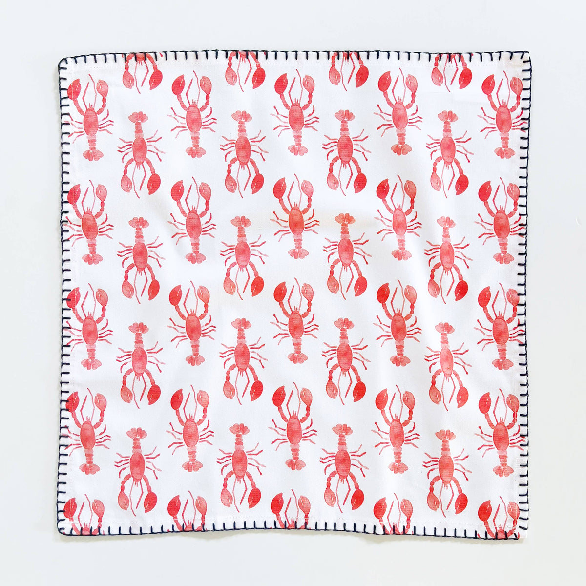 Lobster napkin laid flat showing the full pattern of red lobsters and the navy whipstitch edge