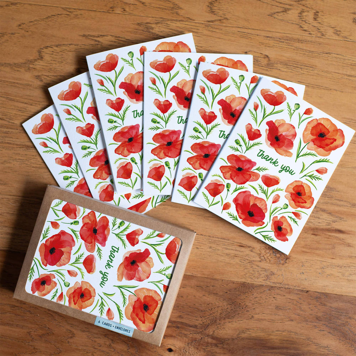 Six Poppy Thank You Cards fanned out on a wood table next to the kraft box labeled 6 cards plus envelopes, red poppies and thank you text visible