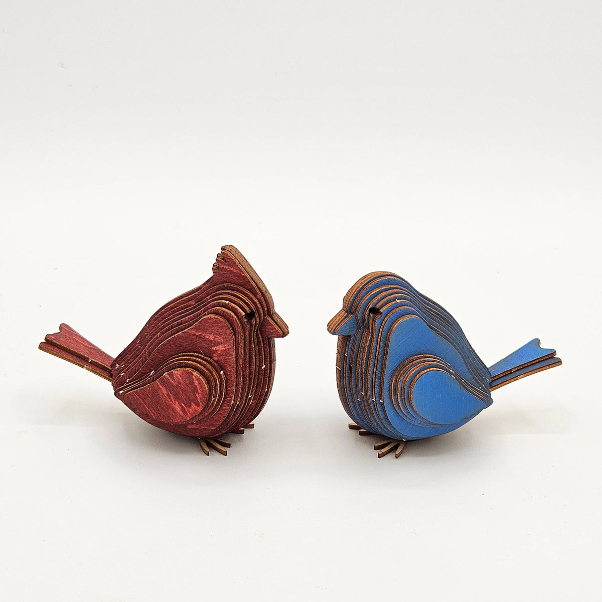 An assembled red cardinal and a blue bird made of layered wood, facing each other