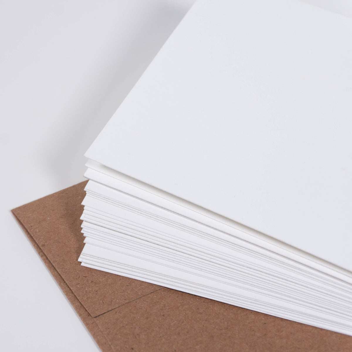 Stack of blank white cards showing the thick cotton paper edges, resting on a kraft envelope