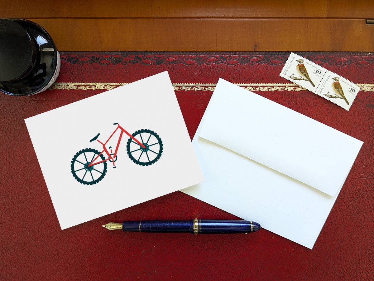 Mountain Bike blank greeting card and white envelope on a red leather desk pad with an inkwell, a fountain pen, and two bird stamps