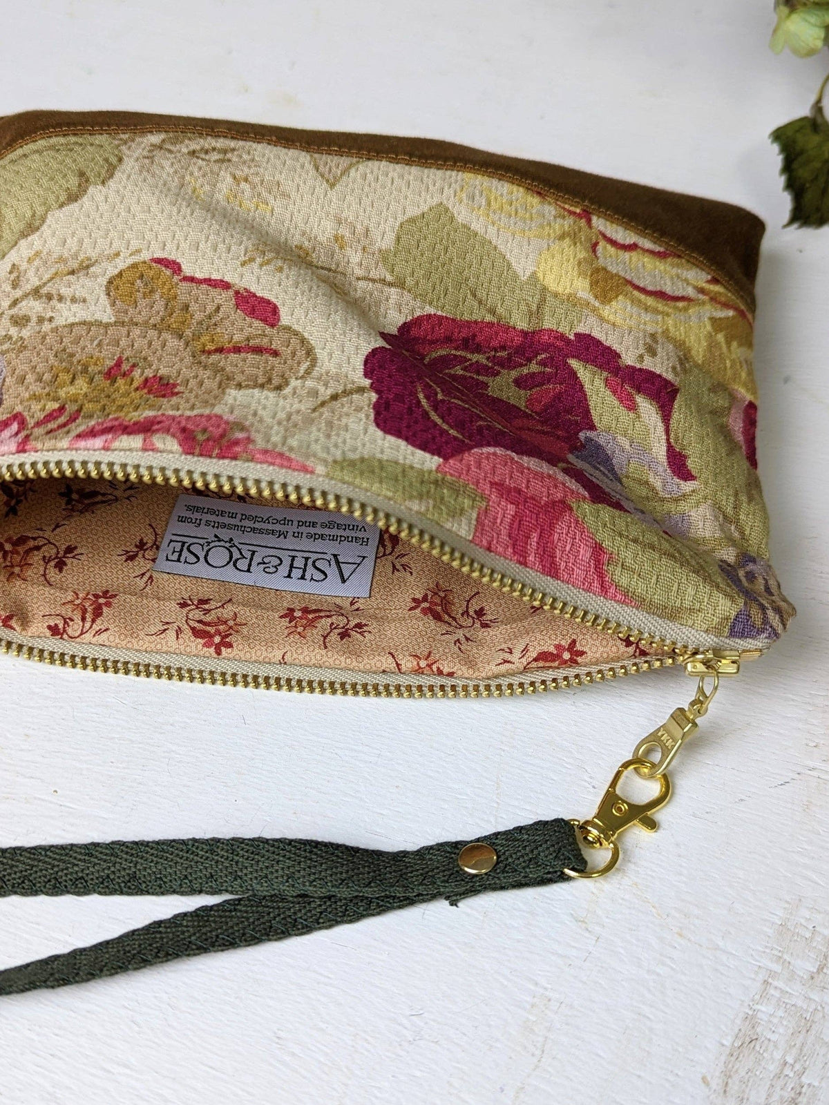 Close-up of Antique Roses wristlet purse exterior, ivory fabric with blue and pink floral pattern bordered by a red stitched vine trim, tan leather bottom