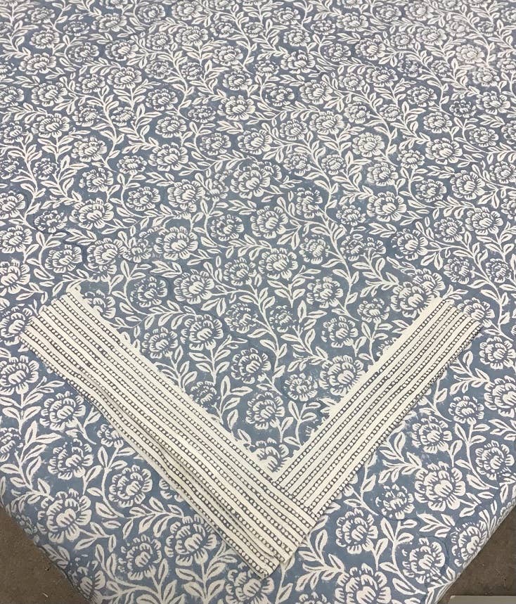 Block-printed napkin with a striped dotted border laid in a corner on a matching blue-gray peony tablecloth