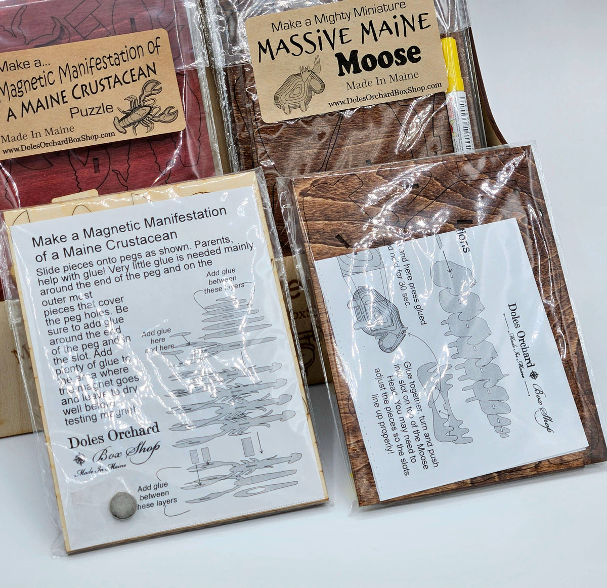 Two puzzle bags with their instruction sheets, a Maine crustacean (lobster) puzzle and a Massive Maine Moose puzzle, with glue and assembly diagrams
