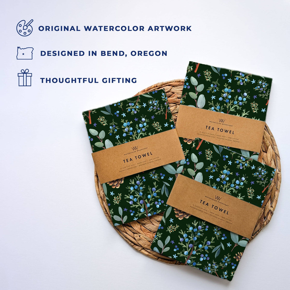 Several folded Winter Juniper Tea Towels wrapped in kraft Watercolor Wednesday tea towel bands on a woven mat