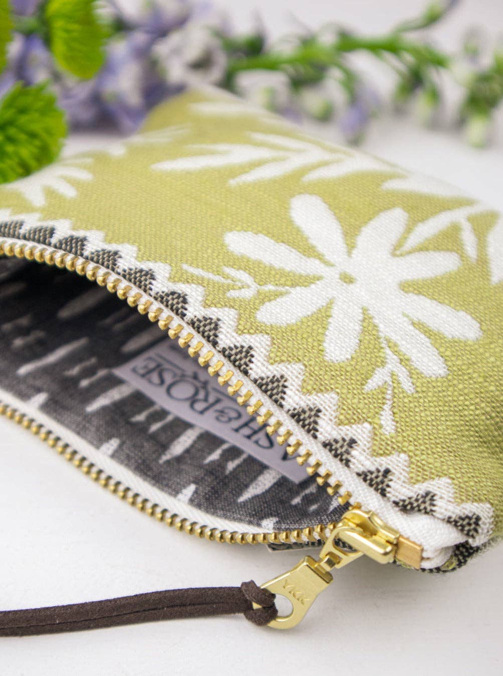 Close-up of an open Folk Life mini pouch showing the Ash & Rose label, olive green daisy-print exterior with black zigzag trim