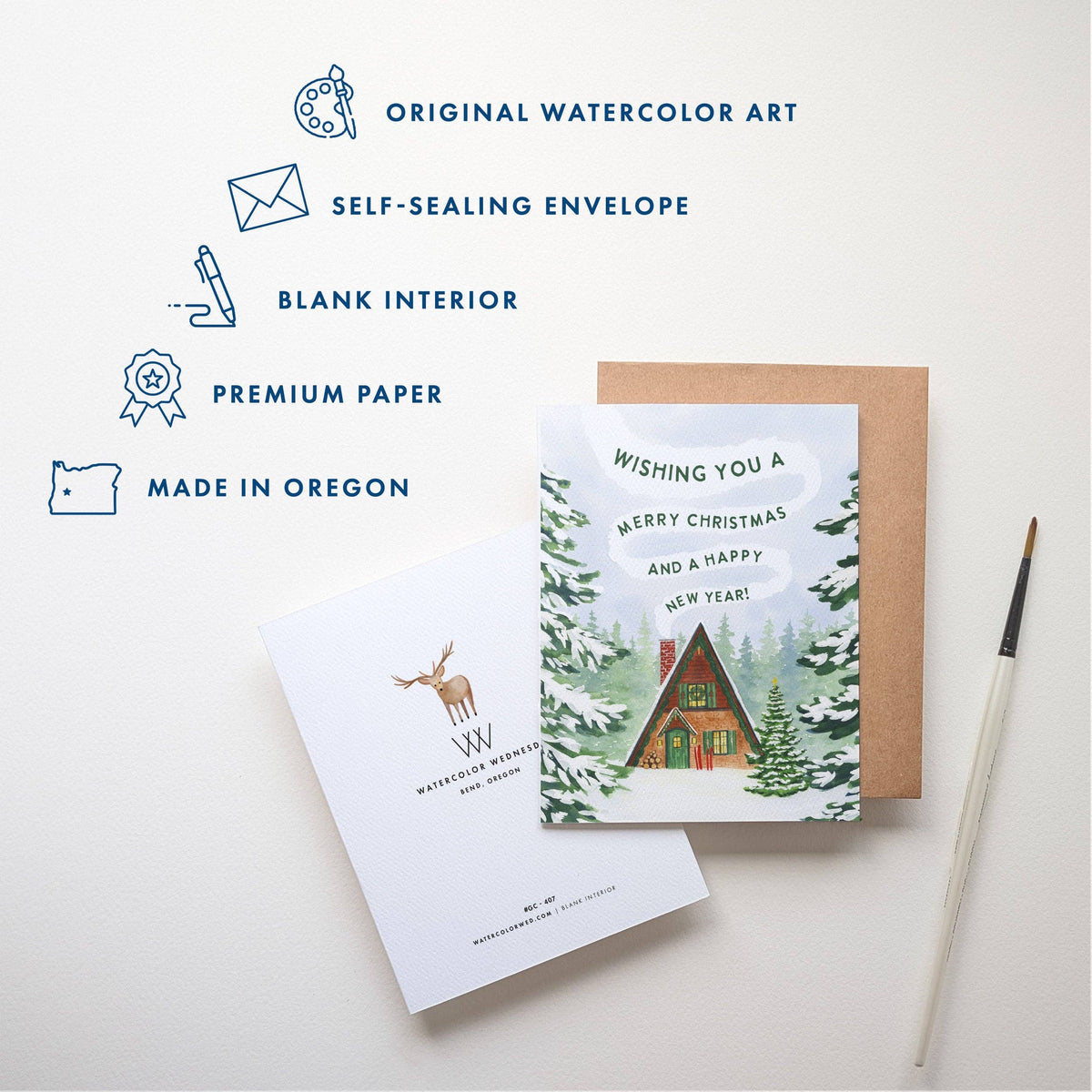 Hands holding the Christmas Cabin Holiday Card over a cozy scene with a knit blanket and an olive green notebook