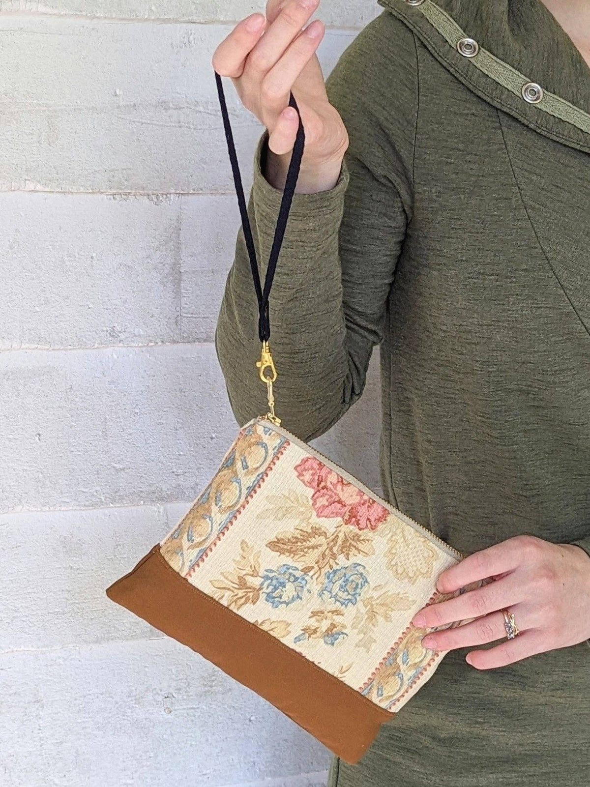 A woman holding an Antique Roses wristlet purse by its black strap, blue and pink floral fabric