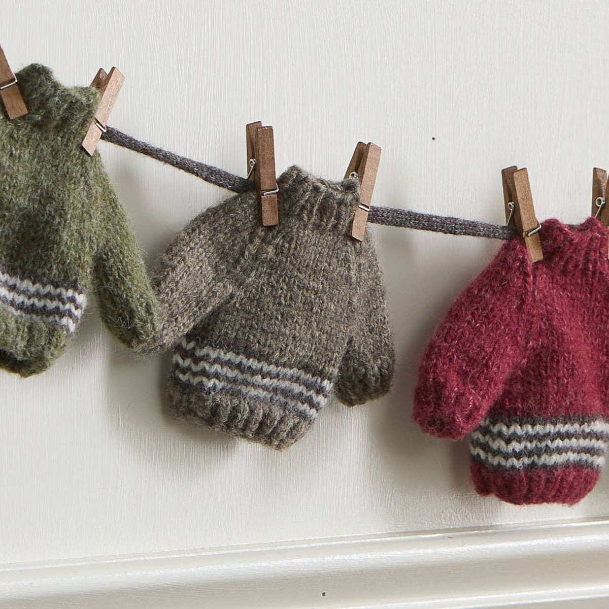 Close-up of tiny knit mittens in green, gray and red hanging from a string with mini wooden clothespins