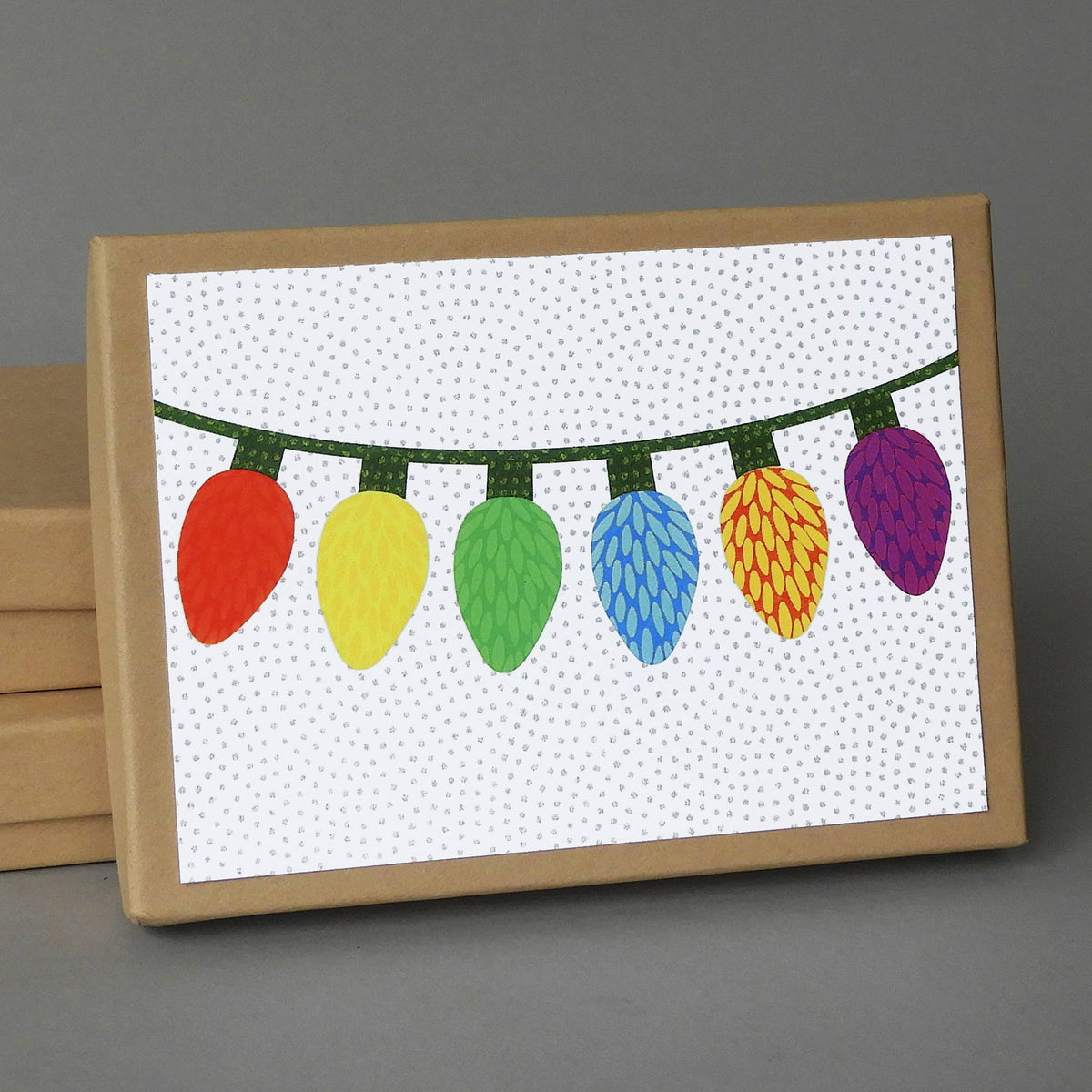 Origami Bulbs Box of 10 blank cards, a kraft box with a string of six multicolored Christmas lights on the lid
