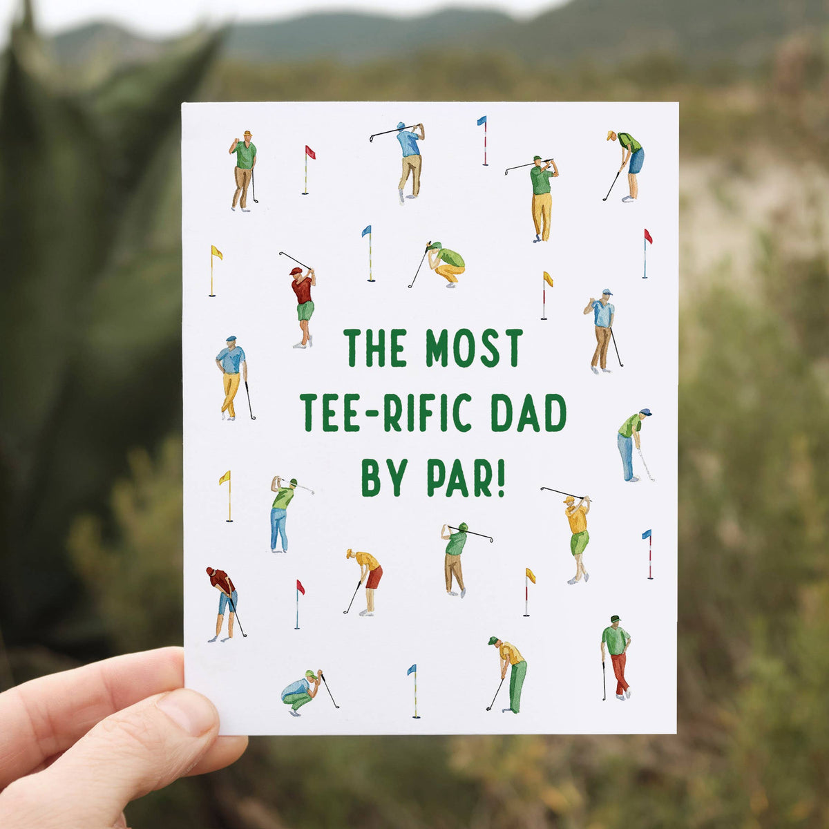 Hand holding the Father Day Card for Golfing Dad outdoors against a blurred green and brown landscape