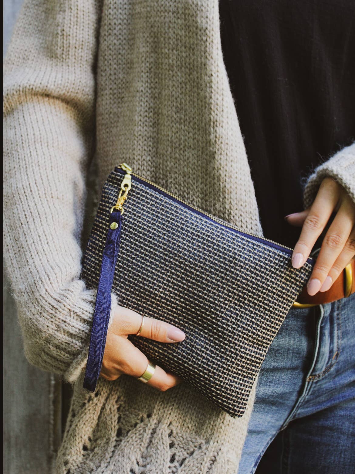 A woman holding a Golden Navy Tweed wristlet purse, navy and gold basketweave pattern, against denim jeans