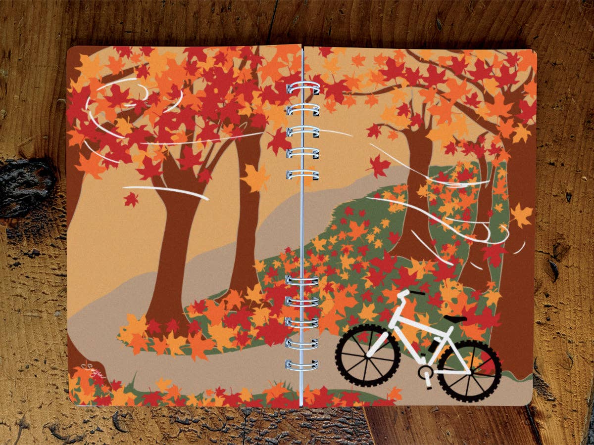 Full wraparound cover of the Autumn Biking spiral notebook: a white mountain bike on a trail among red and orange maple trees and falling leaves