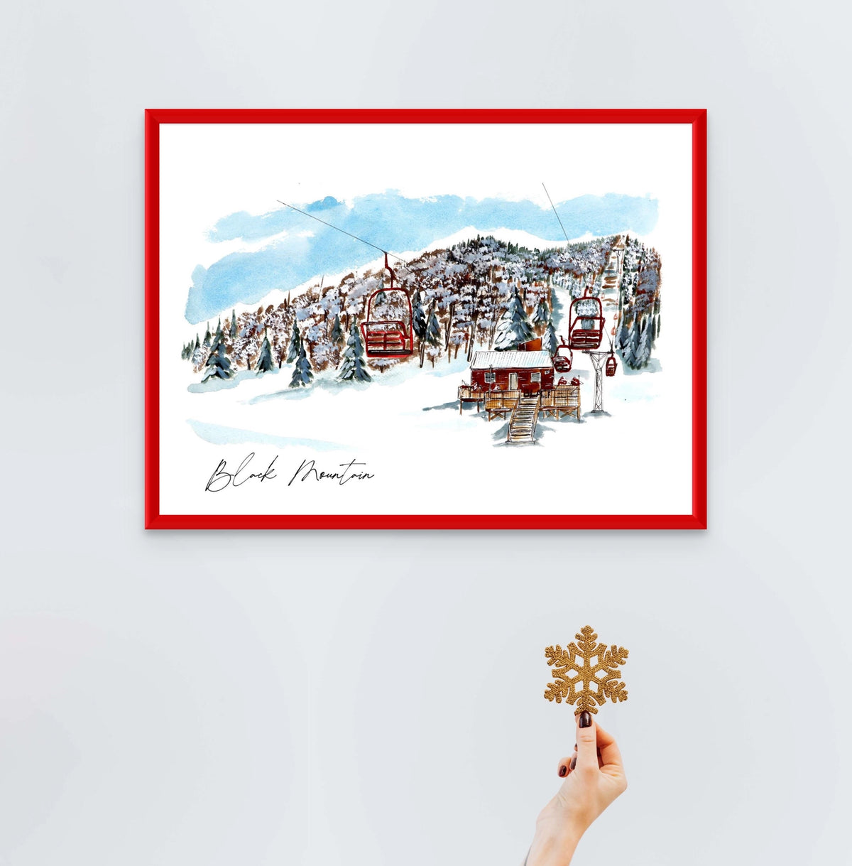 Black Mountain print in a red frame, styled with a hand holding a glitter snowflake ornament