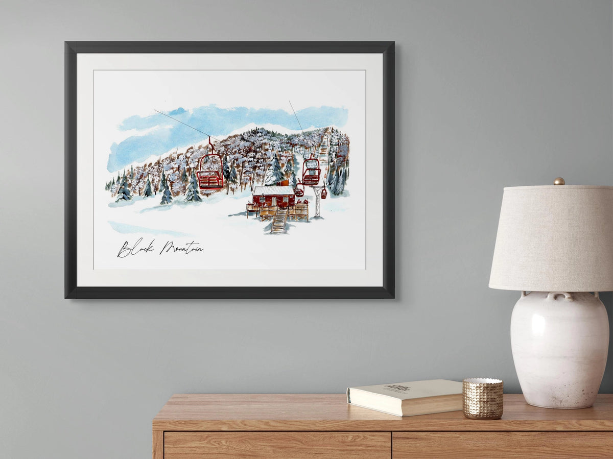 Black Mountain print in a black frame, hung above a wooden dresser styled with a lamp, book, and candle