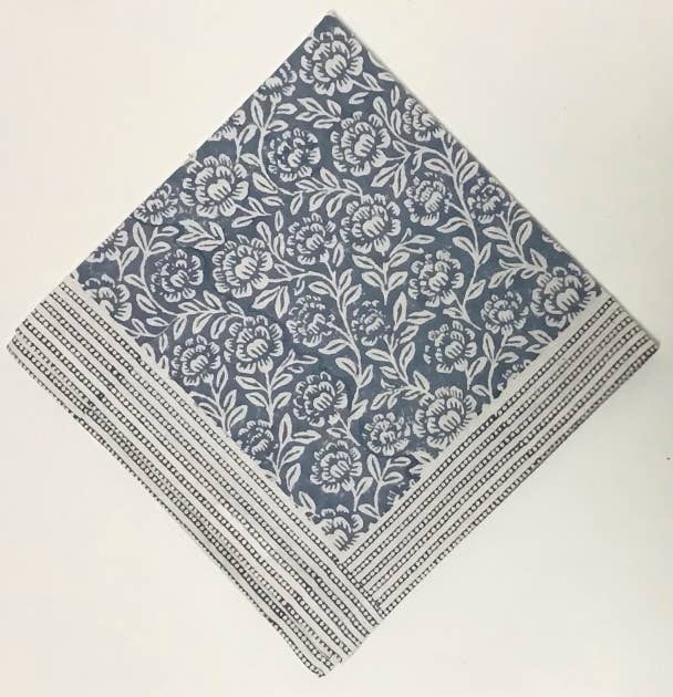 Folded cotton napkin block-printed in blue-gray with a white peony and vine pattern and a dotted stripe border