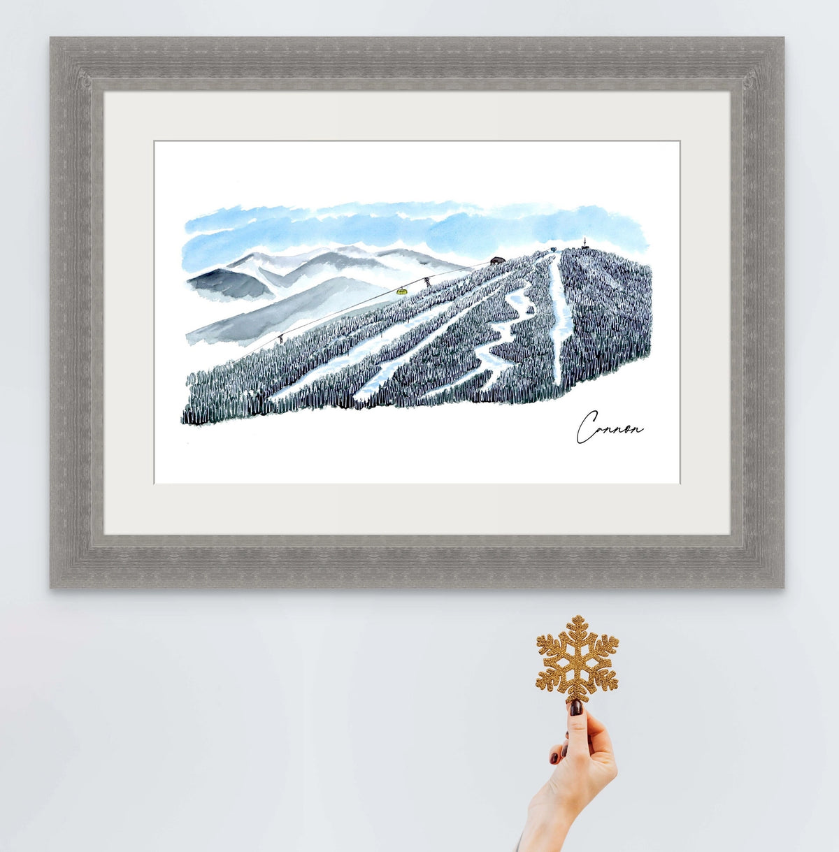 Cannon Mountain trail view print in a grey ornate frame, styled with a hand holding a glitter snowflake ornament