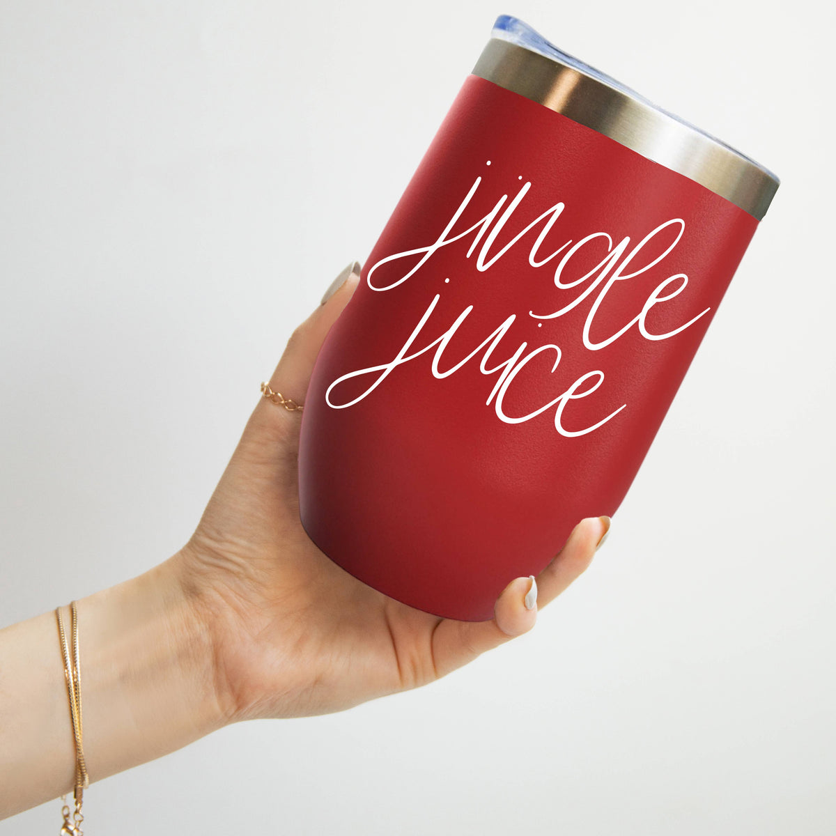 Hand holding a red stainless steel tumbler lettered jingle juice in white script against a light gray background