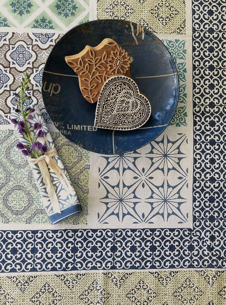 Blue and white block-printed napkin rolled and tied with ribbon and a lavender sprig, on a block-printed tablecloth
