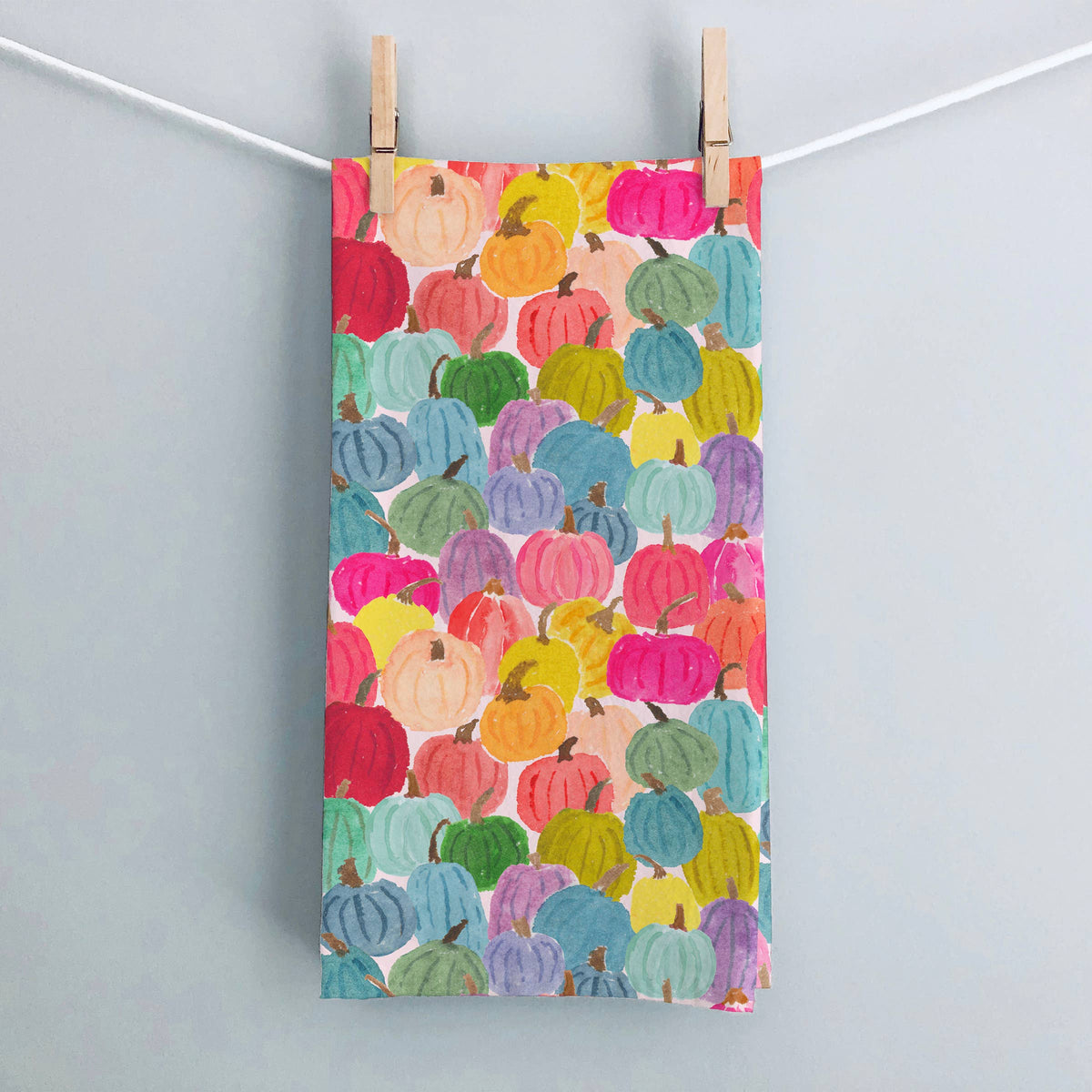 Colorful Pumpkins tea towel hanging from wooden clothespins on a white string against a pale gray wall
